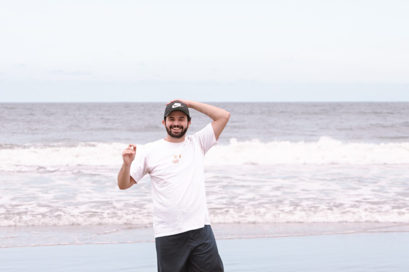 Gabriel T. Godoi sorrindo na praia, de boné e camiseta branca